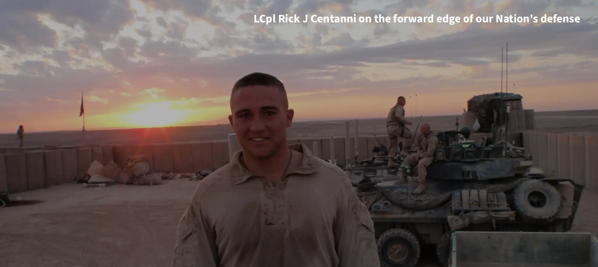 Soldier smiling beside military vehicles at sunset