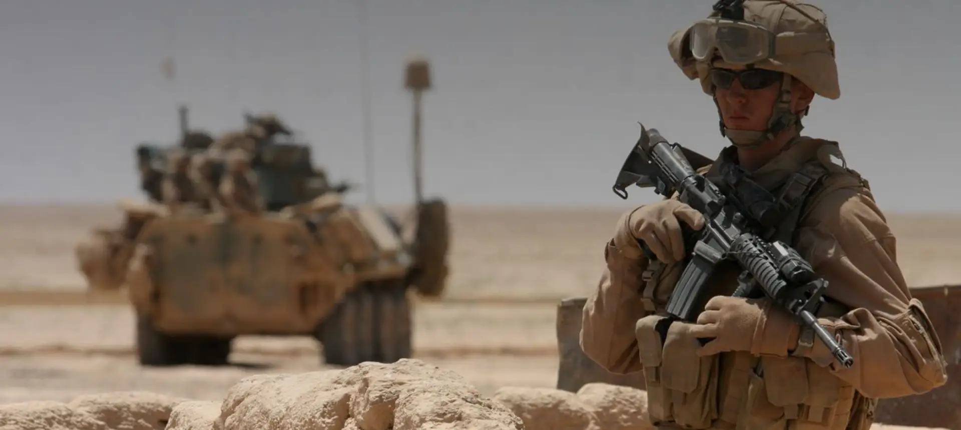 Soldier standing guard in desert near armored vehicle